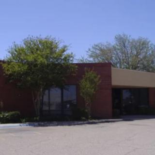 A commercial building with trees and a parking lot under a clear blue sky.