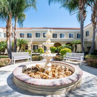 A serene courtyard featuring a central fountain surrounded by benches and palm trees.