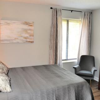 A cozy bedroom with a neatly made bed, modern chair, and window with curtains.