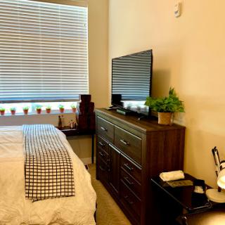 A cozy bedroom featuring a sleek dresser and a television, illuminated by natural light filtering through the blinds.