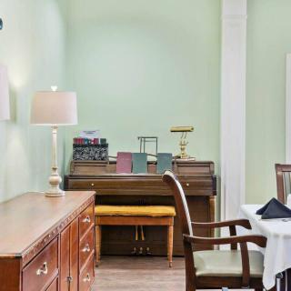 A cozy living room with a wooden desk and chair, surrounded by light green walls and decorated with books and a lamp.