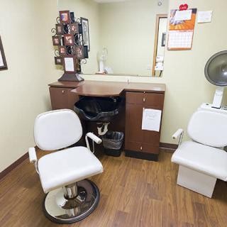 A cozy salon space featuring a styling chair, a mirror, and a hair dryer chair on a wooden floor.