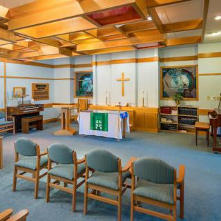 A serene chapel interior with chairs arranged for worship, featuring an altar and a prominent cross.