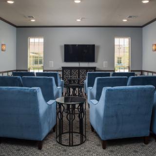 A cozy theater room with blue chairs arranged facing a wall-mounted television.