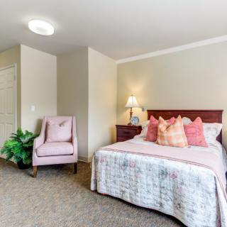 A cozy bedroom featuring a bed with decorative pillows, a bedside lamp, and an upholstered chair.