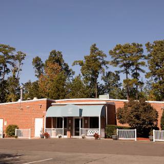 A brick building surrounded by trees, featuring a canopy and a parking lot.