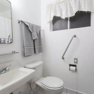 A clean, white bathroom with a sink, mirror, towels, and a grab bar next to the toilet.