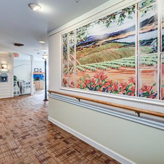 A well-lit hallway featuring a large landscape painting and wooden flooring.