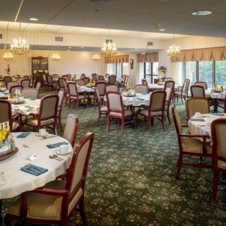 Elegant dining room with arranged tables and chairs, featuring chandeliers and a carpeted floor.