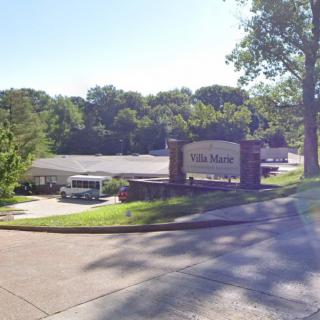 Entrance to a facility surrounded by trees with a visible sign and road.