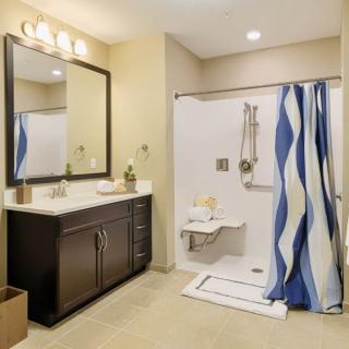 A modern bathroom featuring a wide mirror, dark vanity, and accessible shower with a blue striped curtain.