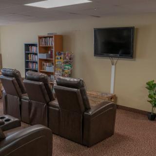 A cozy home theater setup with recliner chairs facing a wall-mounted TV and a bookshelf in the background.