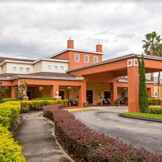 A large building with a covered entrance and landscaped surroundings under a cloudy sky.