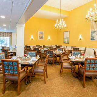An elegant dining room interior with multiple tables and chairs, decorated with chandeliers and bright yellow walls.