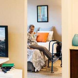 An elderly person in a cozy bedroom, using a walker for support.