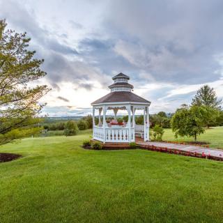 A scenic view of a gazebo surrounded by lush greenery and a cloudy sky.
