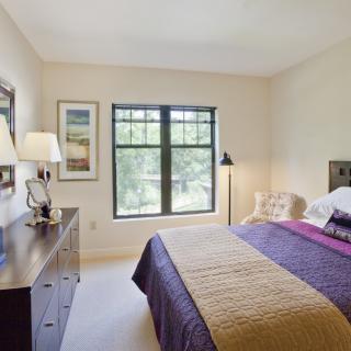 A cozy bedroom with a large window and neatly arranged furniture.