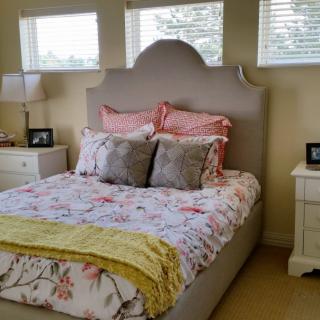 A cozy bedroom with a neatly made bed featuring floral bedding and decorative pillows, flanked by white nightstands and lamps.