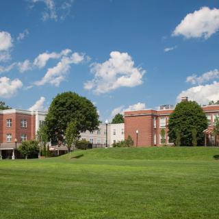 A scenic view of a college campus with brick buildings, a large grassy field, and a clear blue sky.