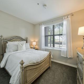 A cozy bedroom featuring a wooden bed, soft white bedding, and natural light filtering through the window.