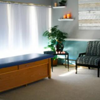 A serene massage room with a therapy table, comfortable chair, and soothing decor.