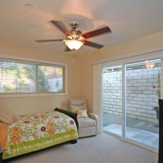 A cozy bedroom with a ceiling fan, single bed, comfortable chair, and sliding patio door.