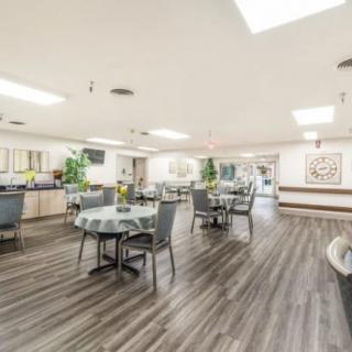 A spacious dining room with several tables and chairs, featuring hardwood flooring and bright interior lighting.