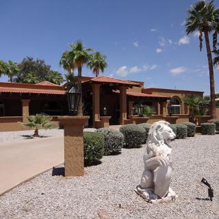 A residential building surrounded by palm trees and desert-themed landscaping, featuring a prominent lion statue in the foreground.