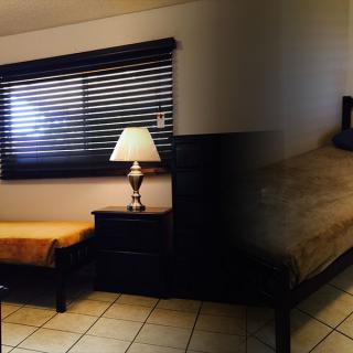 A cozy bedroom with a bed, nightstand, lamp, and window with blinds.