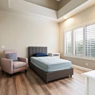 A minimalist bedroom with a single bed, armchair, and wooden flooring.