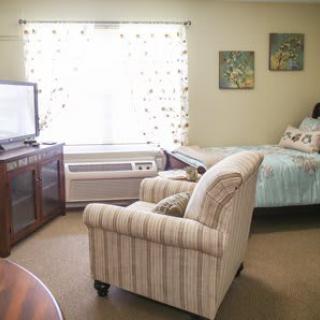 A cozy living space featuring a TV, armchair, and bed with natural light coming through the window.