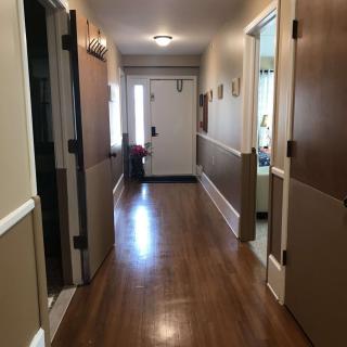 A well-lit residential hallway with wooden flooring and doors leading to various rooms.