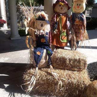 Festive autumn decorations featuring cheerful scarecrows sitting on hay bales.
