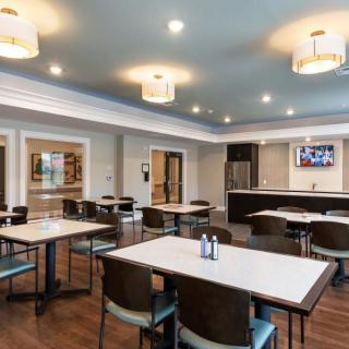 A modern dining area with neatly arranged tables and chairs, featuring stylish lighting and a kitchen setup in the background.