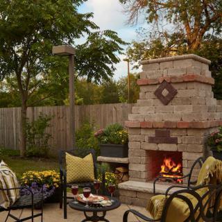A cozy outdoor patio with a stone fireplace, surrounded by comfortable seating and lush greenery.