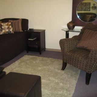 A cozy living room with a patterned chair, sofa, small table, and a rug.