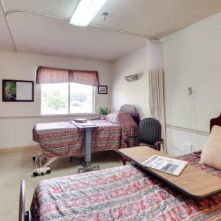 A cozy hospital patient room featuring two beds, a window with curtains, and a small table.