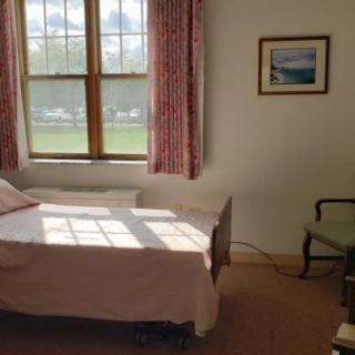 A cozy bedroom with a bed, window, and curtains, illuminated by natural light.