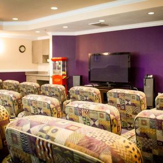 A cozy home theater setup with patterned seating facing a large television on a purple accent wall.