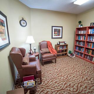 A cozy office space with armchairs, a bookshelf filled with books, and warm lighting.