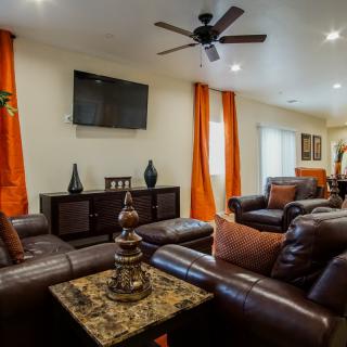 A modern living room featuring leather sofas, a television, and bright orange curtains.
