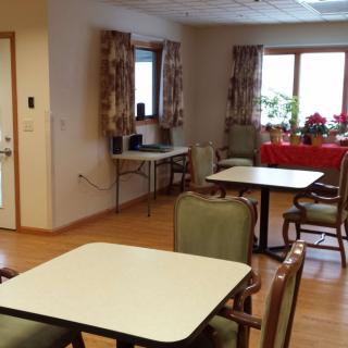 A dining area with tables and chairs, featuring windows with curtains.
