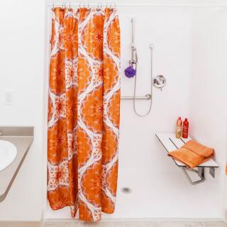 A modern bathroom featuring an orange patterned shower curtain and a folding seat.
