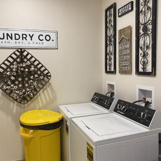 A cozy laundry room with washing machines, decorative wall art, and a bright yellow trash can.