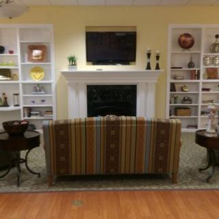A cozy living room with a striped sofa facing a fireplace, flanked by bookshelves and a wall-mounted television.