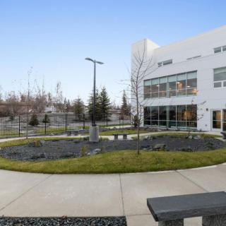 A modern building with a landscaped garden and trees under a clear sky.
