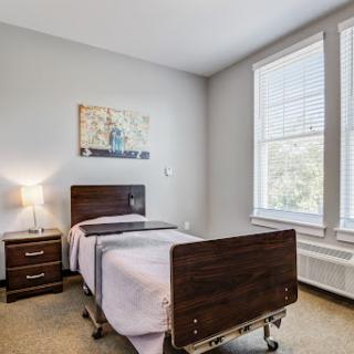 A well-lit patient room featuring a hospital bed, nightstand, and natural light from the window.