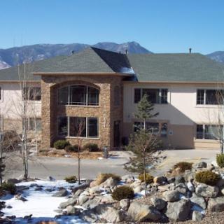 A beautiful residential building set against a mountainous backdrop, surrounded by landscaped rocks and snow.