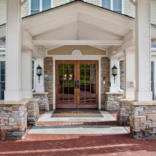 A welcoming building entrance featuring stone columns, a brick pathway, and double wooden doors.