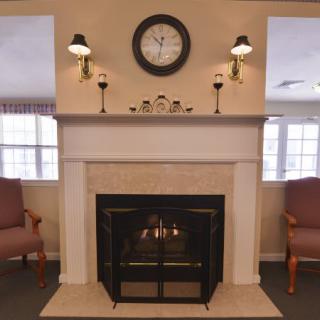 A cozy living room with a fireplace and armchairs, featuring a clock above the mantel.